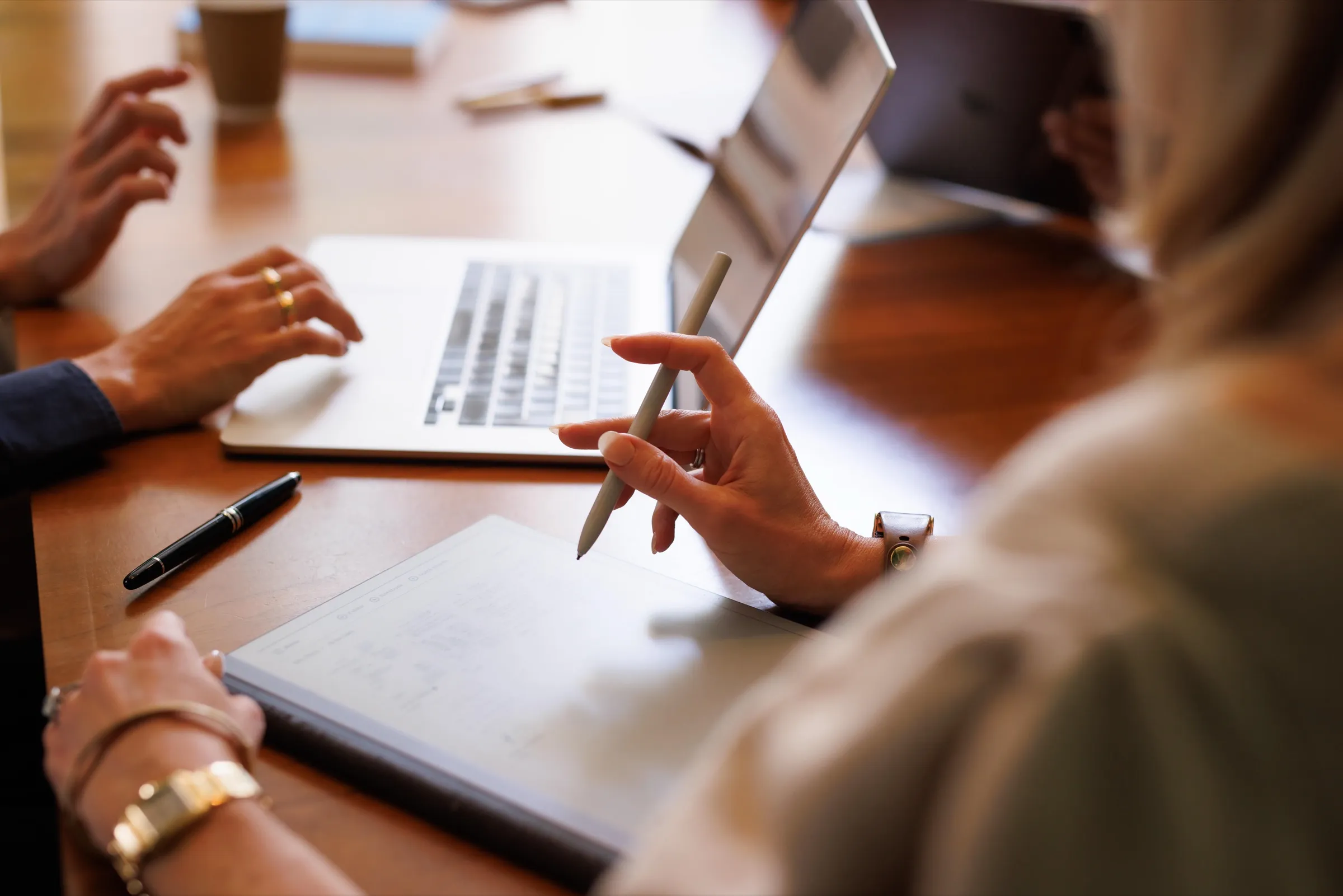 Hands with a stylus, tablet and laptop during a meeting